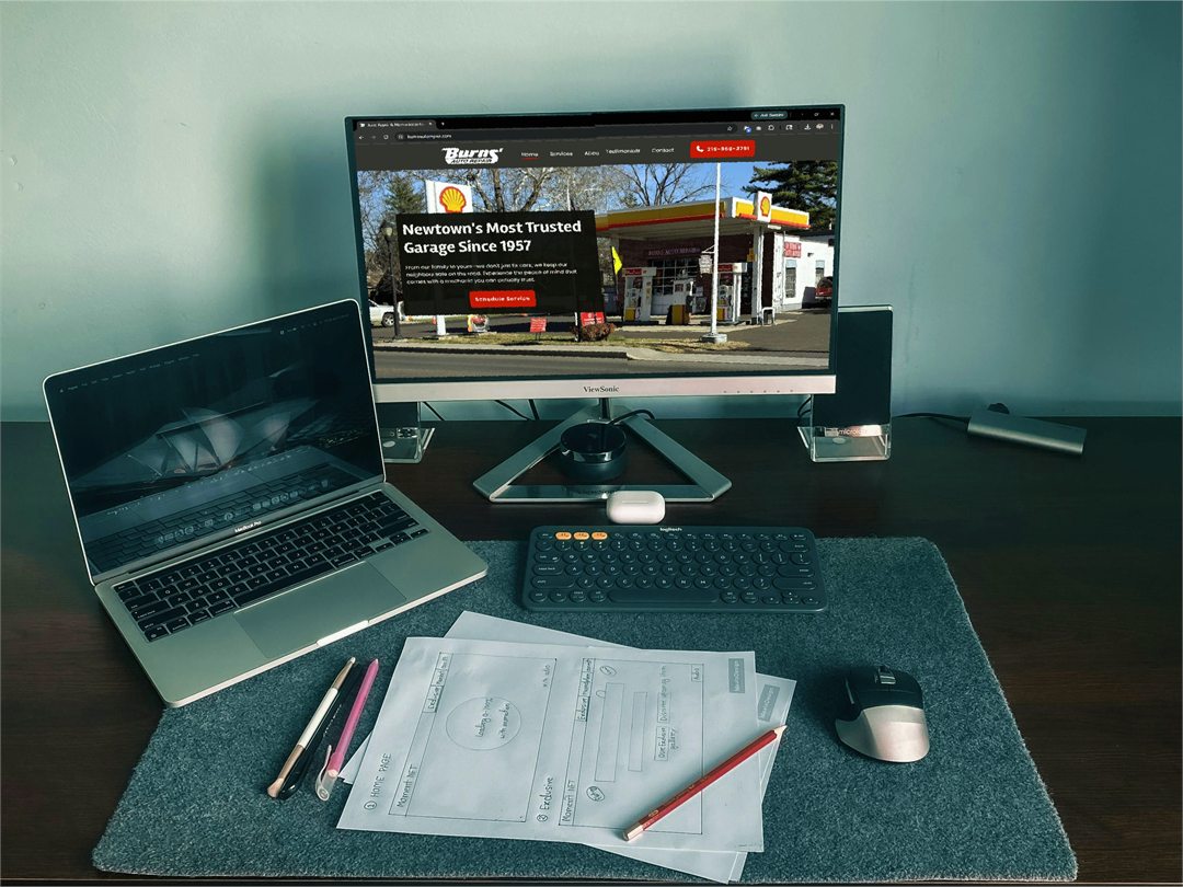 desktop showing a notebook, a laptop, and a monitor with Burns' Auto Repair website open
